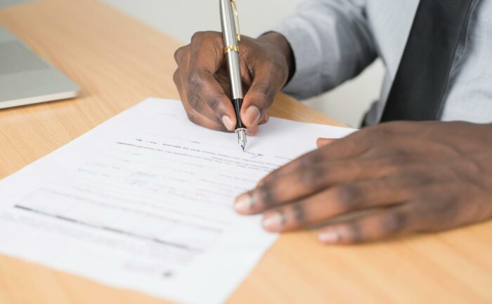 person holding gray twist pen and white printer paper on brown wooden table